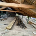 A pile of decayed rafters that have been removed from the external canopy. Several new timbers lie next to them. The roof has been almost completely replaced with fresh, new timbers.
